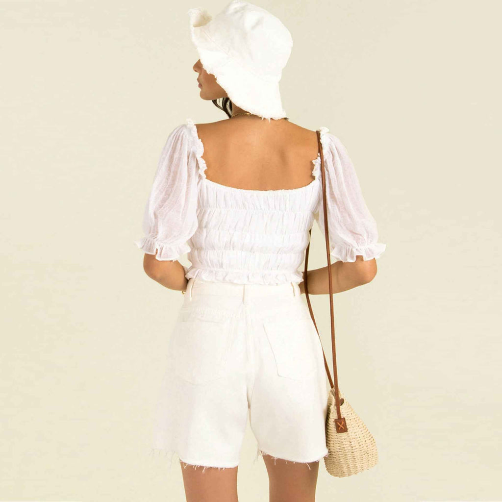 Back view of a woman wearing a white summer pleated lantern sleeve top with a hat and shorts